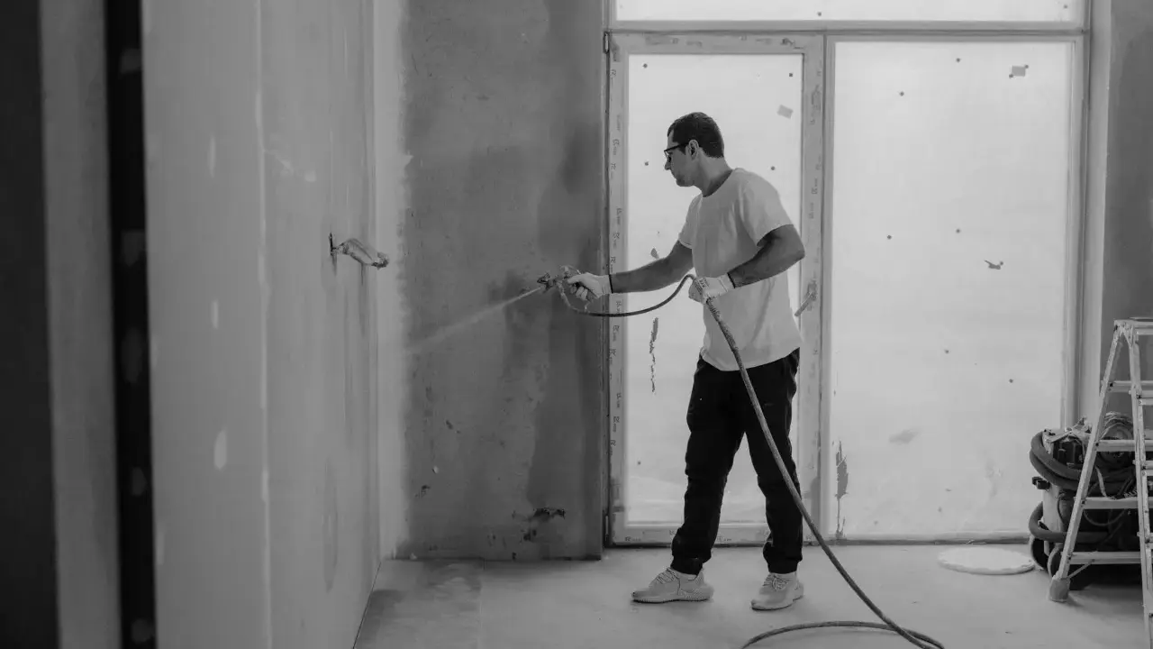 Man sprutar färg på en vägg inomhus, en del av arbetet med fasad hus.