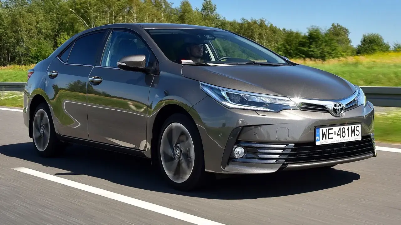Szara Toyota Corolla E16 jedzie po drodze, za kierownicą siedzi mężczyzna.