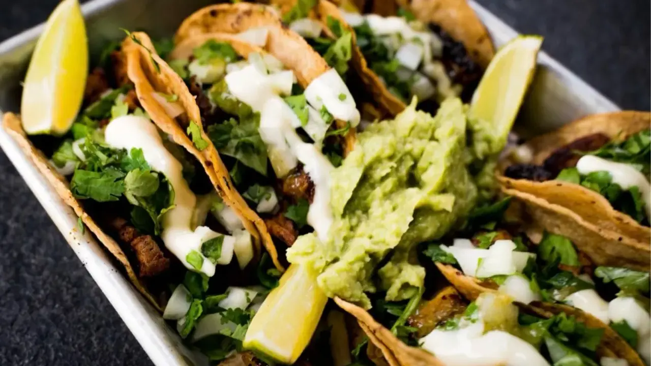 Saftige Tacos al Pastor mit Guacamole, Koriander und Limettenspalten.