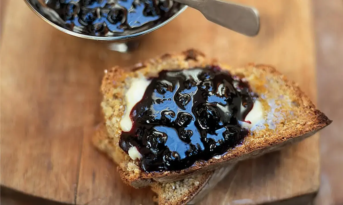 Ein Toast mit Butter und ausgefallener Heidelbeermarmelade, die in einem silbernen Schälchen daneben serviert wird.