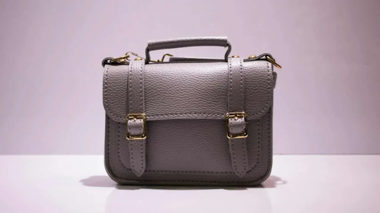 Graue Handtasche mit goldenen Schnallen und Griff. Perfekt, um Ihre wichtigsten Dinge zu handtasche organisieren.