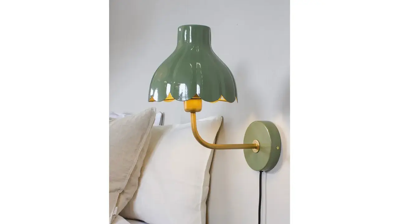 A green scalloped lampshade with a yellow interior, mounted on a gold arm attached to a green wall plate.