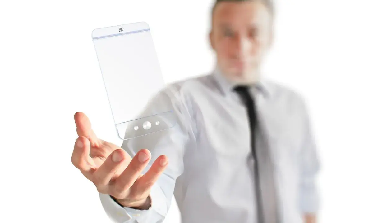 Mężczyzna w białej koszuli i krawacie trzyma w dłoni przezroczysty telefon, symbol przyszłości technologii.