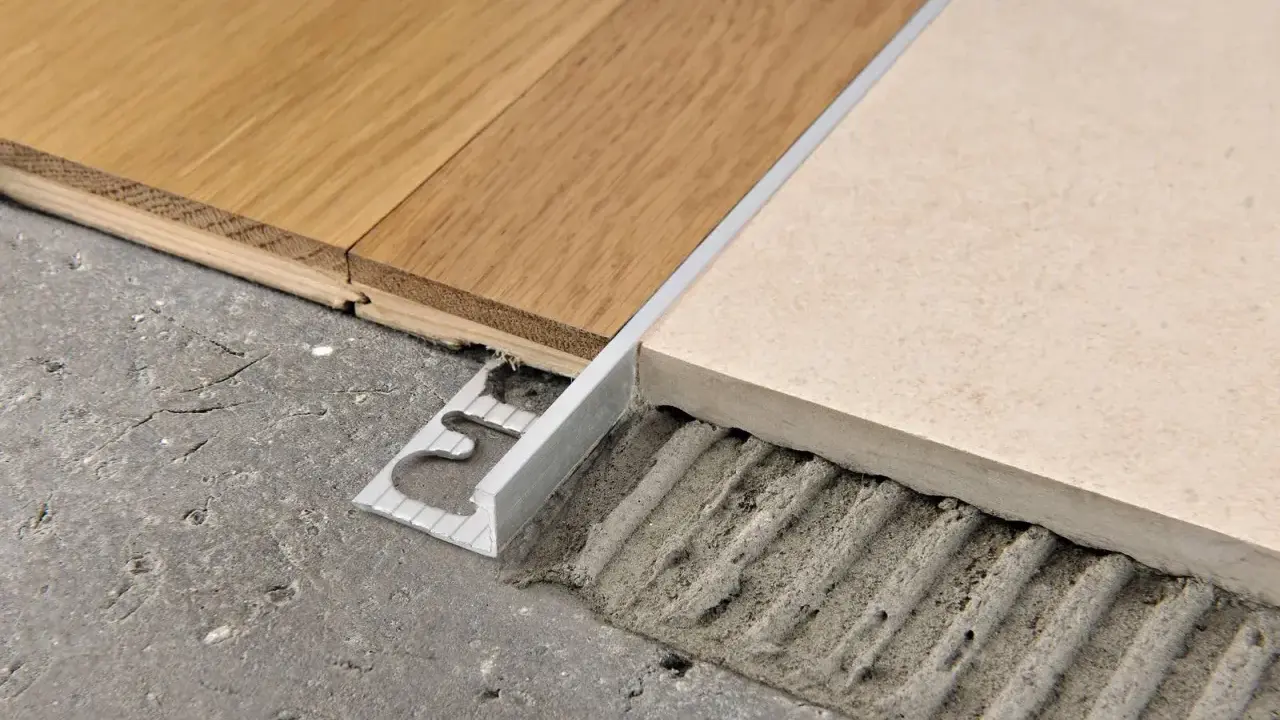 Un battiscopa metallico crea abbinamenti quando mancano le piastrelle del pavimento, unendo legno e ceramica su un sottofondo grezzo.