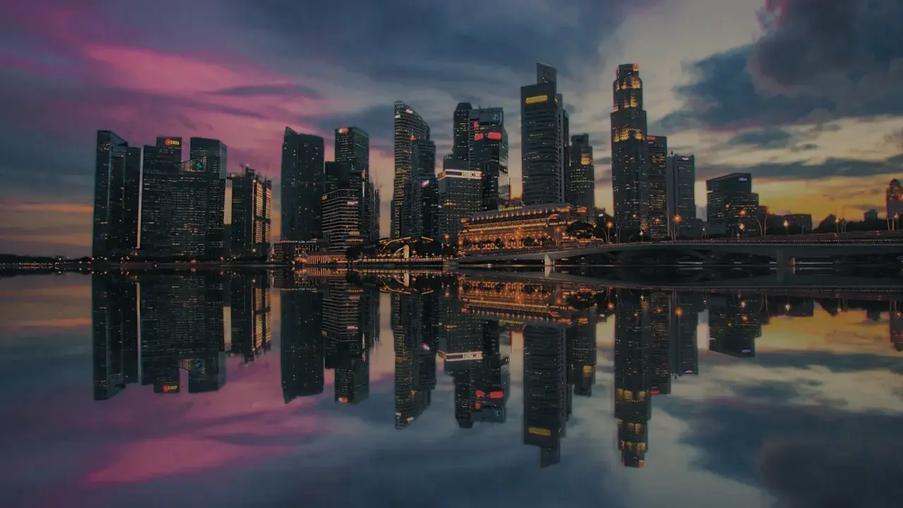 Wieżowce w Singapurze odbijają się w wodzie o zachodzie słońca. To miasto-państwo, gdzie leży Singapur, zachwyca nowoczesną architekturą.