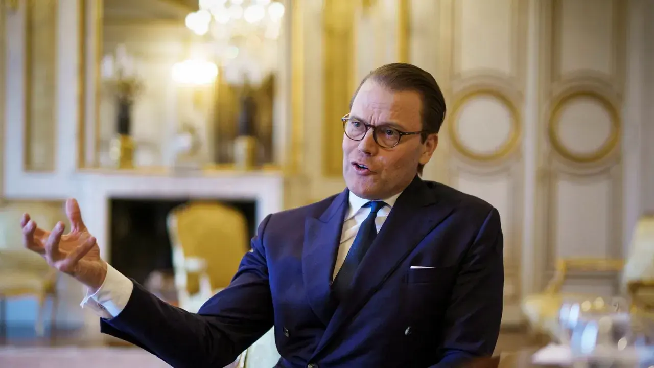 Prins Daniel i mörk kostym, med glasögon, gestikulerar. Rykten om prins Daniel otrogen sprids.