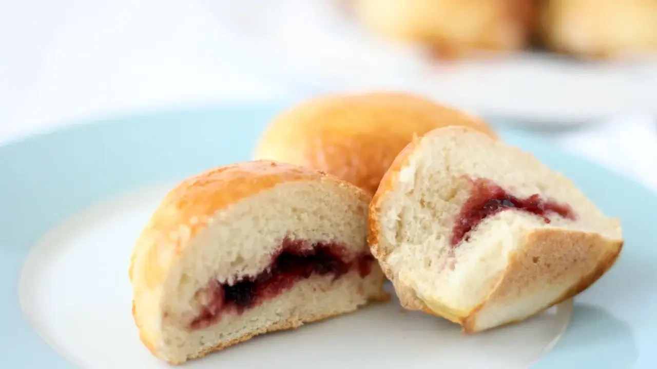Dos bollos dorados, uno cortado, revelan un relleno de mermelada de fresa. ¡Un dulce bocado!