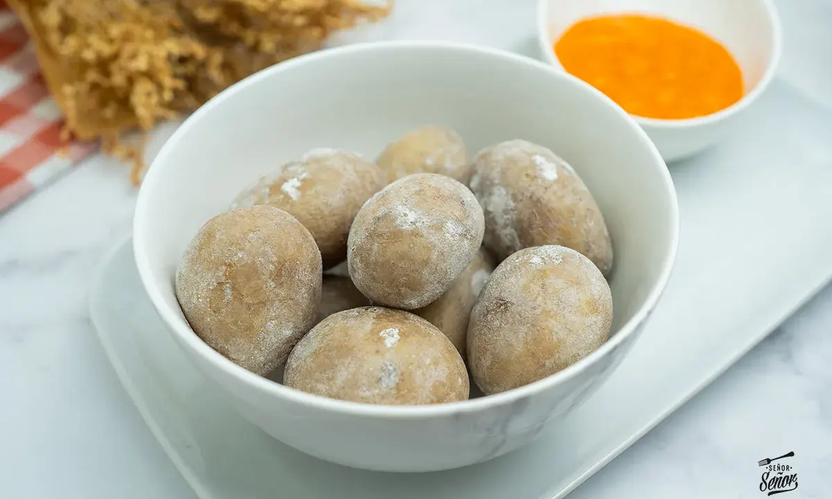 Un tazón blanco lleno de papas arrugadas, cubiertas de sal, junto a un pequeño cuenco con mojo rojo.