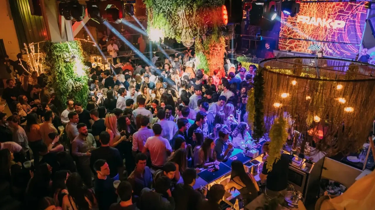 Menschen tanzen und feiern in einem belebten Club in Lissabon. Grüne Pflanzen und Lichter schaffen eine lebendige Atmosphäre.