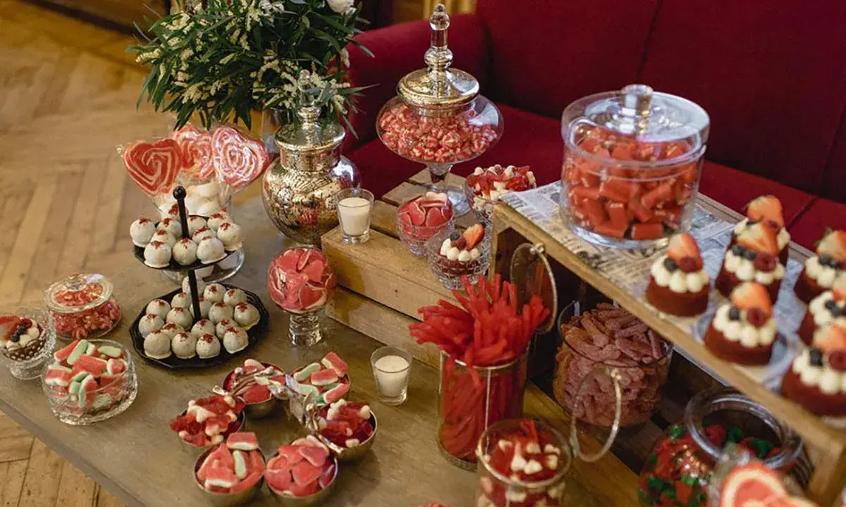 Un candy bar boda casero lleno de dulces rojos y rosas, piruletas, pasteles y golosinas.