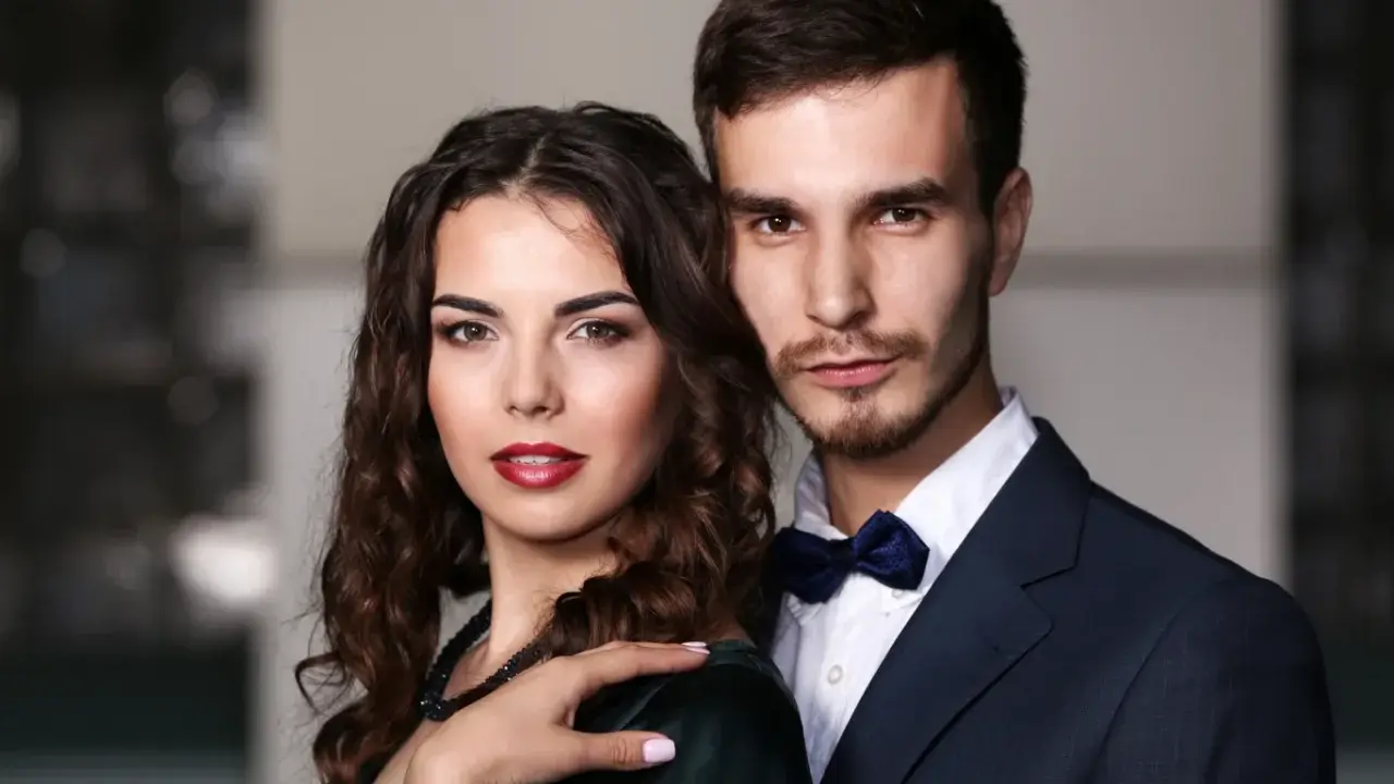 Elegancka para, niczym koziorożec i baran, pozuje do zdjęcia. Ona w ciemnej sukni, on w granatowym garniturze.