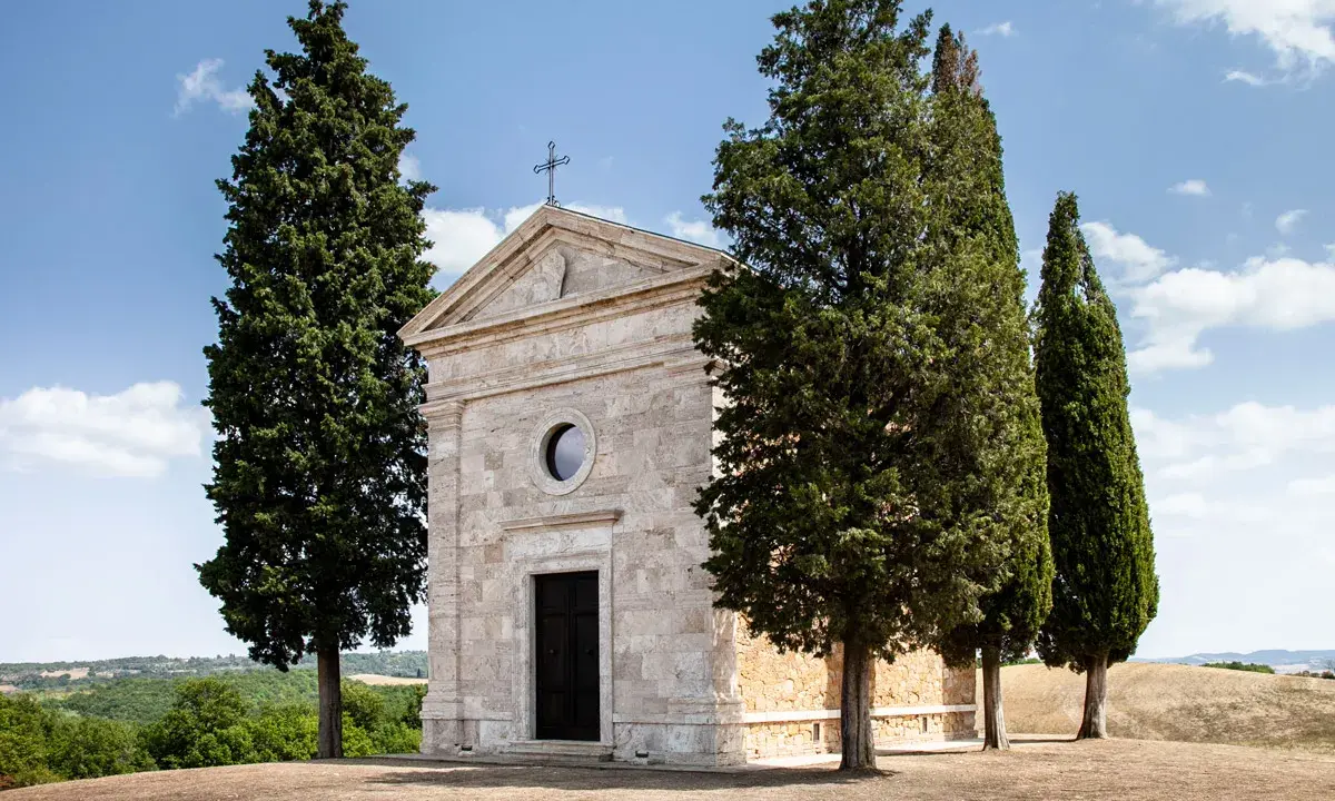 La chiesa di Vitaleta, con i suoi cipressi iconici, si erge solitaria su una collina toscana sotto un cielo azzurro.