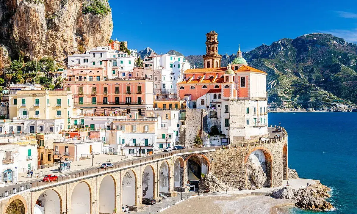 Un incantevole borgo da visitare in Campania, con case colorate aggrappate alla roccia, un ponte ad archi e il mare blu.