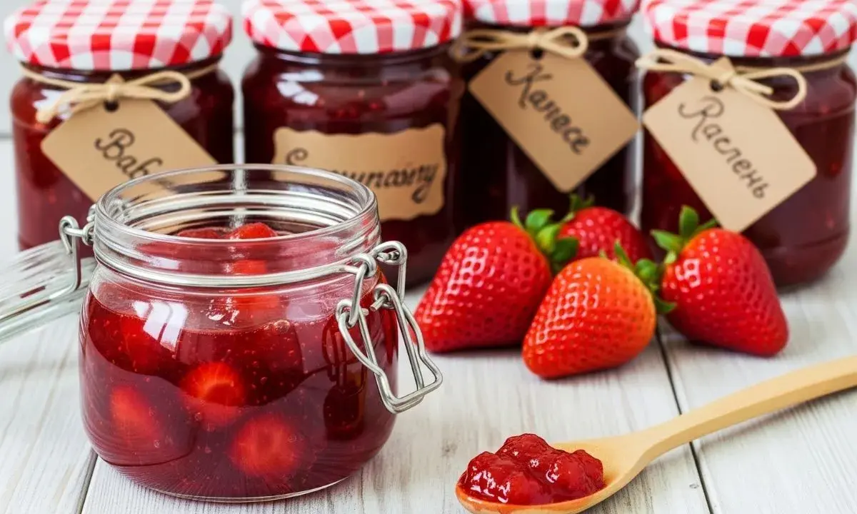 Bocaux de confiture de fraise faits maison, avec des fraises fraîches et une cuillère remplie de confiture.