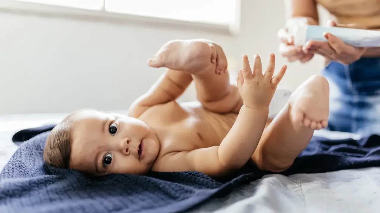 Uroczy noworodek leży na granatowym kocyku, podnosząc nóżki. Mama przygotowuje się do masażu brzuszka, by ulżyć mu w **gazach u noworodka**.