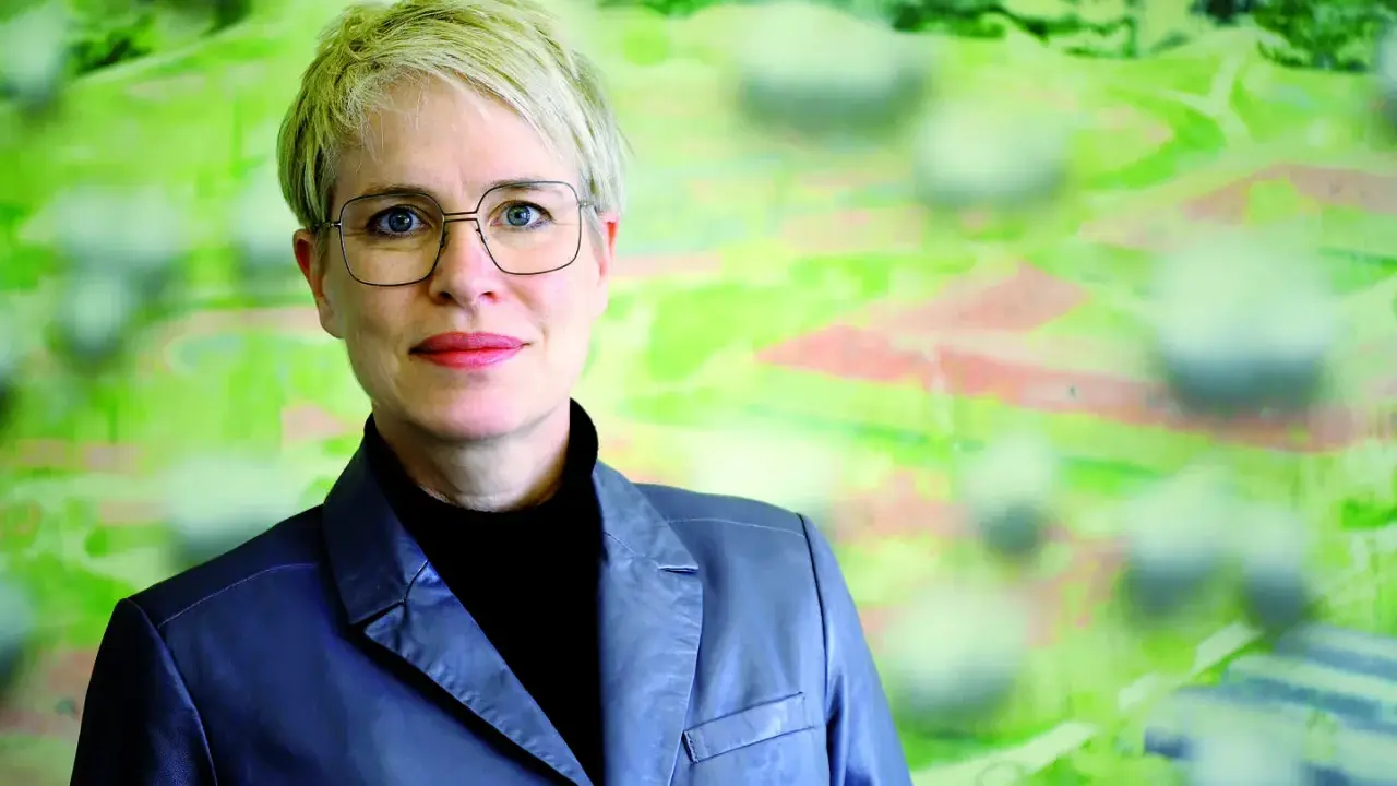 Frauke Burgdorff, eine Frau mit kurzen blonden Haaren und Brille, blickt lächelnd in die Kamera. Sie trägt einen grauen Blazer.