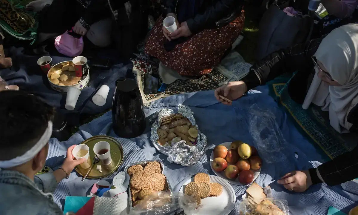 Familie feiert Fastenbrechen im Islam mit Picknick im Freien. Kekse, Früchte und Kaffee werden geteilt.
