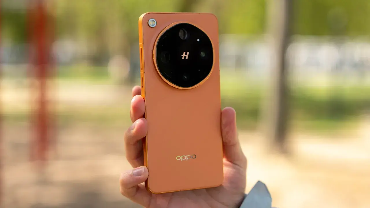 Pomarańczowy oppo flagowiec z charakterystycznym modułem aparatu w dłoni, na tle rozmytego, zielonego krajobrazu.