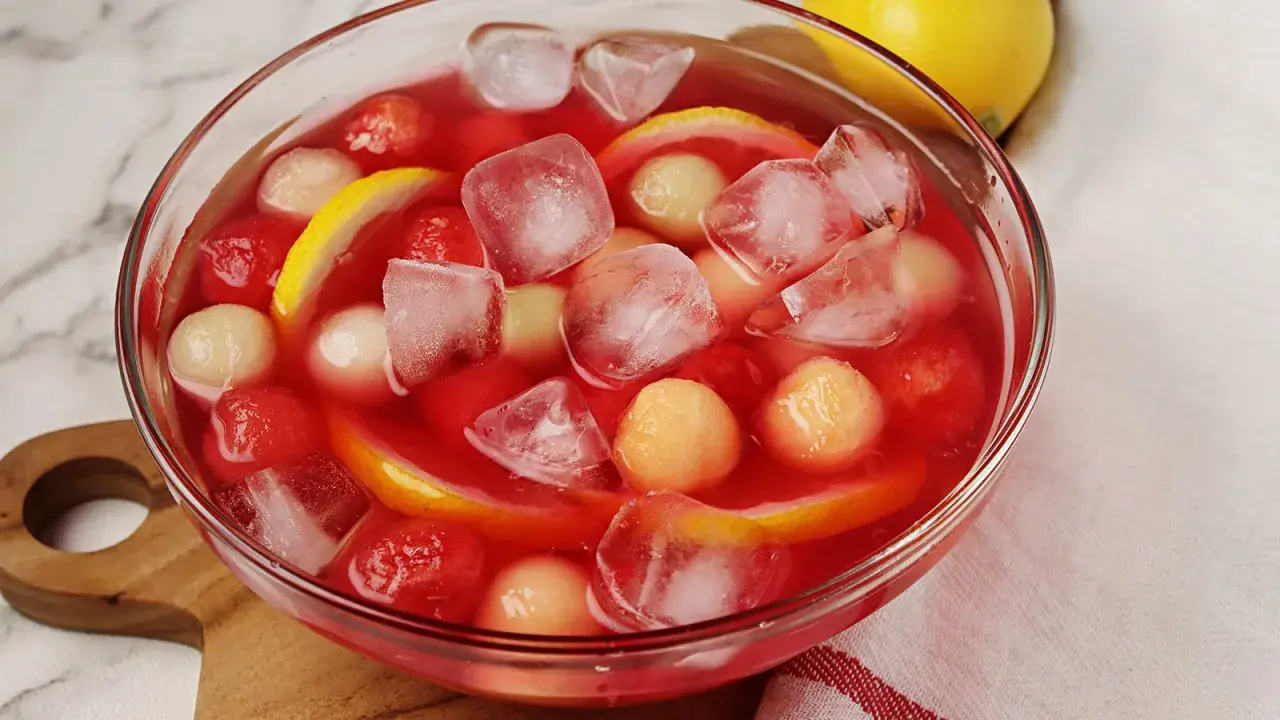 Erfrischende melonenbowle ohne alkohol mit Eiswürfeln, Melonenbällchen und Zitronenscheiben in einer Glasschüssel.
