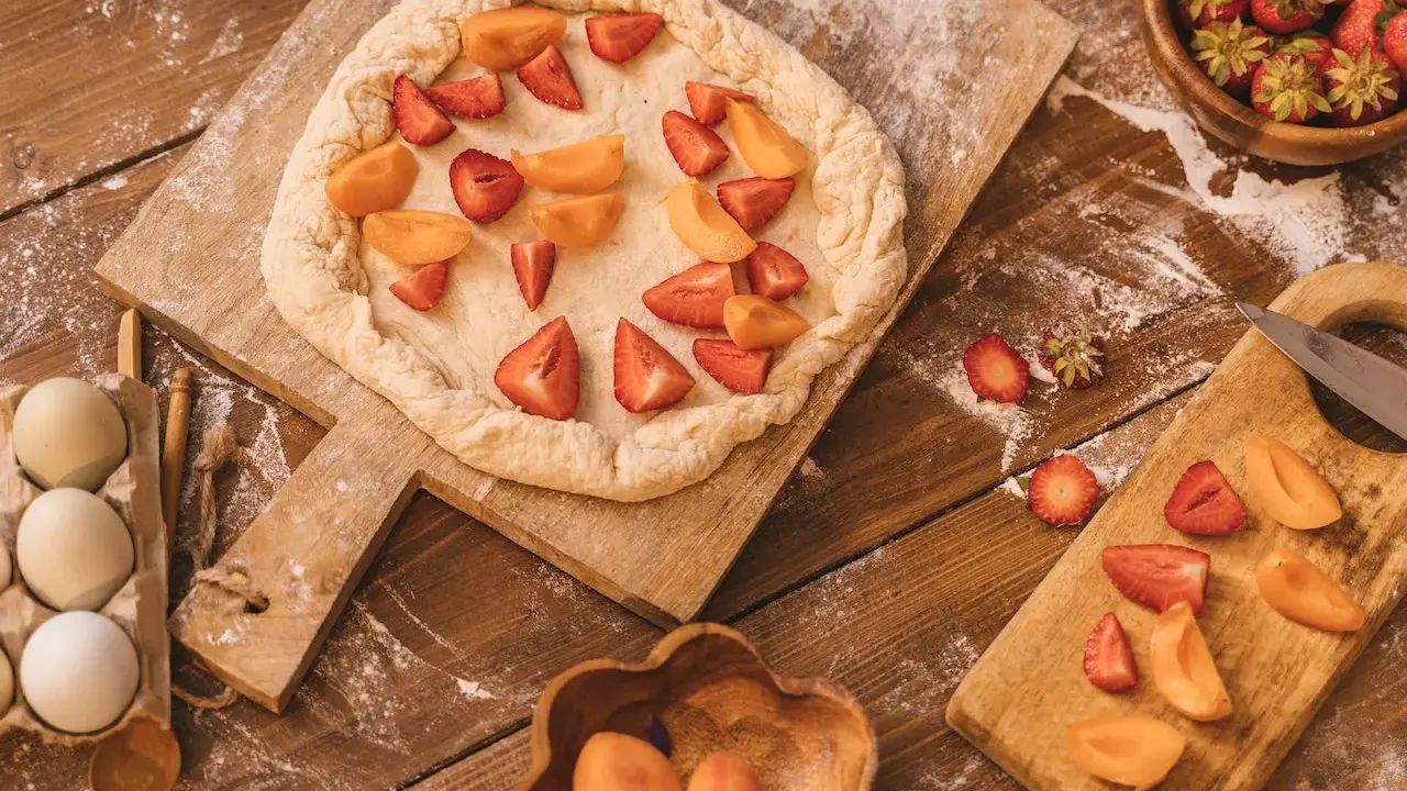 Préparation d'un crumble abricot et fraises sur une planche en bois, avec des œufs et des fruits frais à proximité.