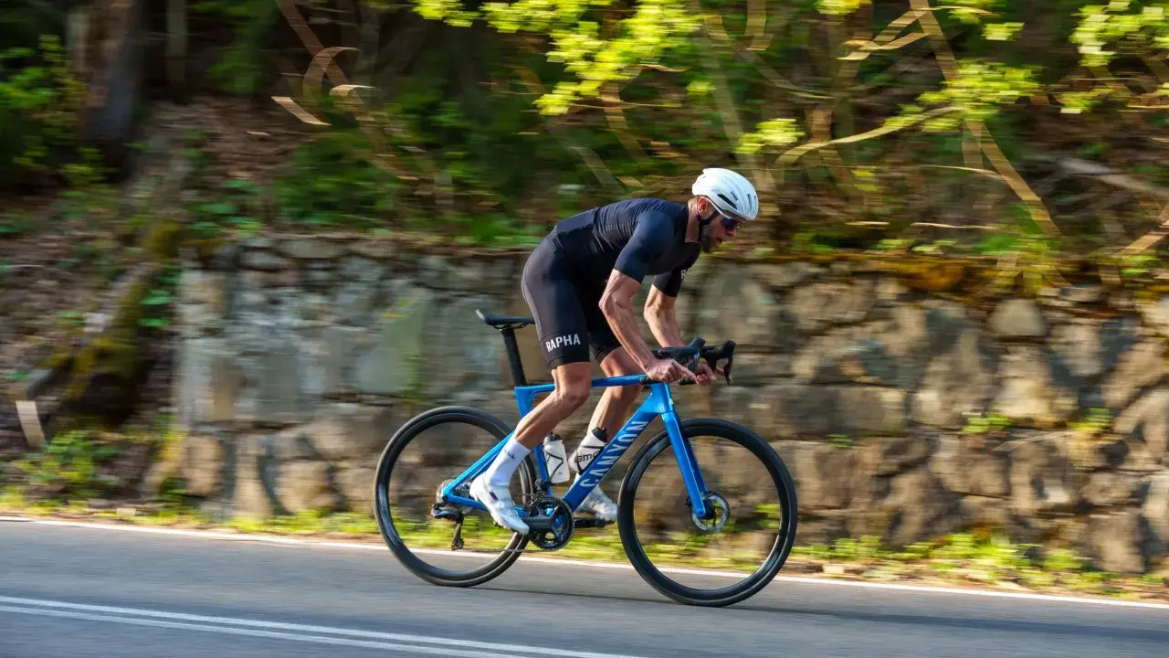 Kolarz w kasku ściga się na niebieskim rowerze Canyon Endurace CF 7 po malowniczej drodze wśród zieleni.