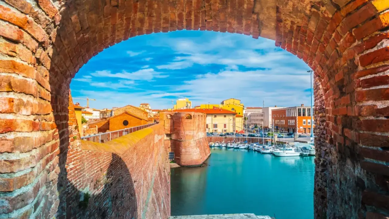 Widok na port w Livorno przez ceglany łuk. Widać łodzie, budynki i fortyfikacje. Idealne miejsce, by zobaczyć Livorno.