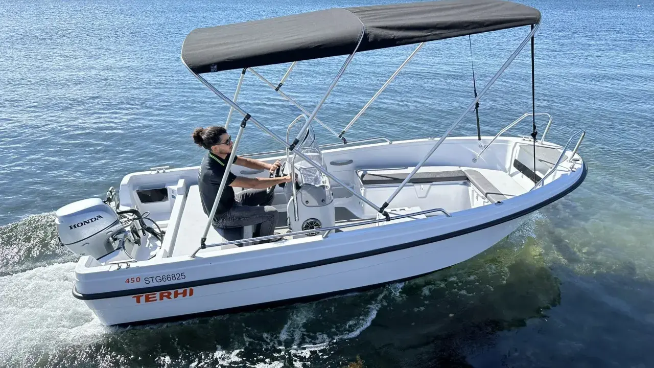 Ce bateau Terhi 450, propulsé par un moteur Honda de 6 cv, navigue sur une mer calme. Idéal pour explorer les côtes.