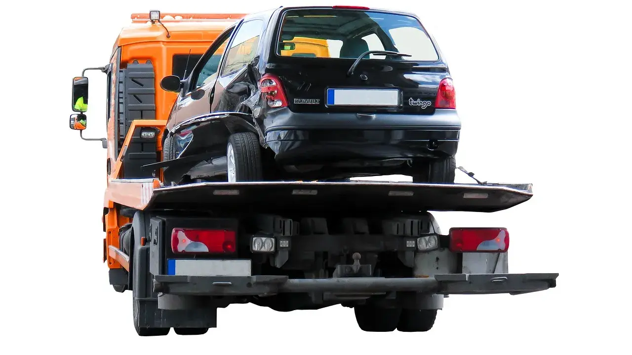 Pomoc drogowa pokazuje, jak holować auto po wypadku. Uszkodzony czarny Renault Twingo jest ładowany na lawetę.