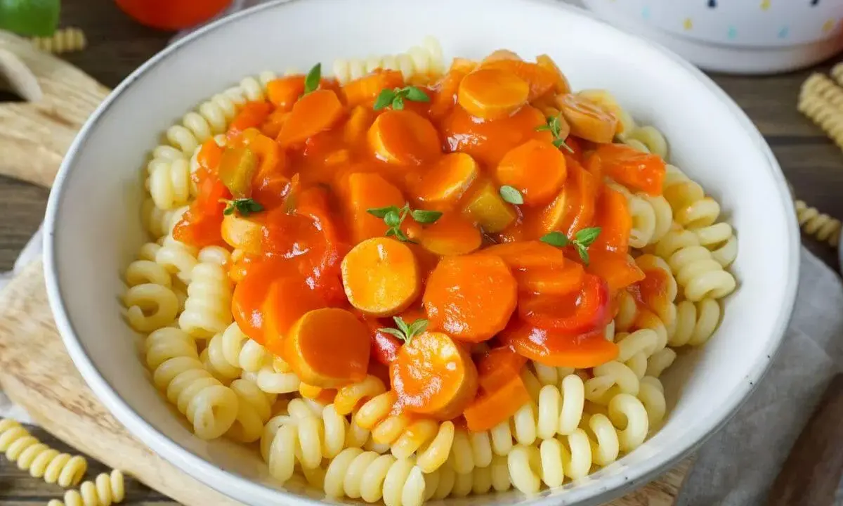 Herzhaftes Wurstgulasch Rezept mit Fusilli-Nudeln, Karotten und Paprika in Tomatensauce, garniert mit frischen Kräutern.