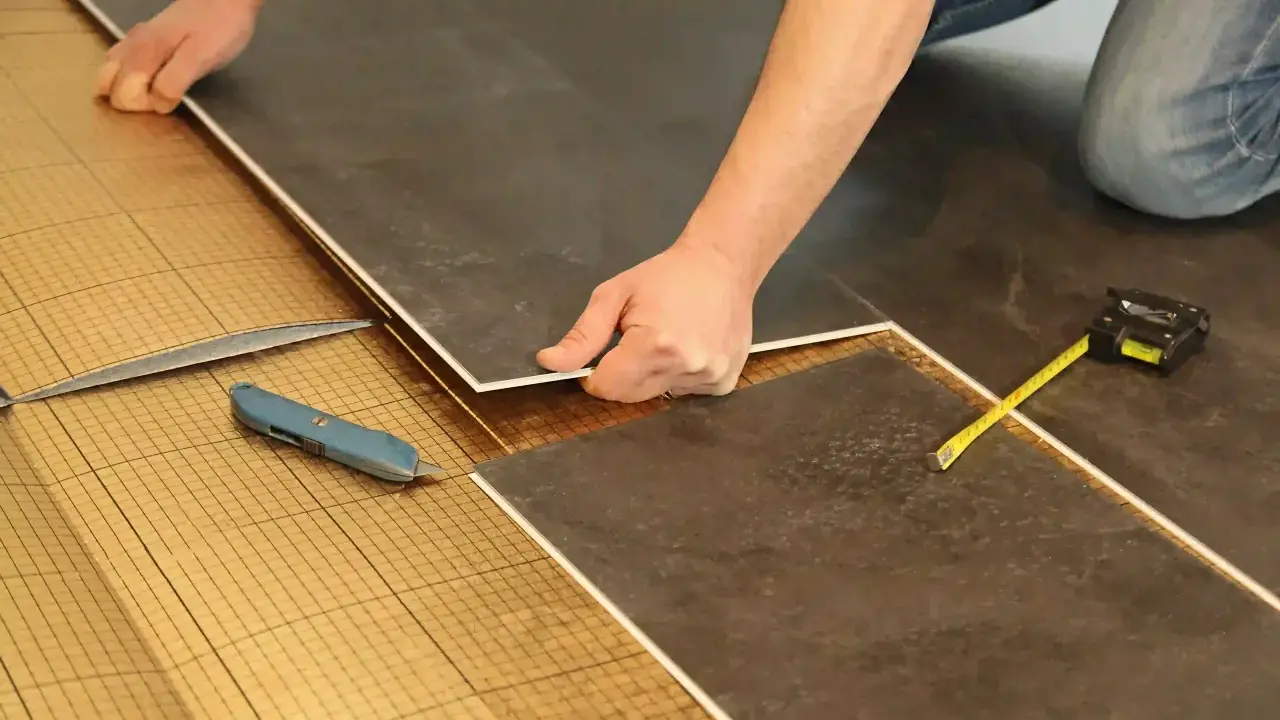 Pose de dalles de sol sur une sous-couche isolante. Un cutter et un mètre sont à portée de main pour comment isoler un sol efficacement.