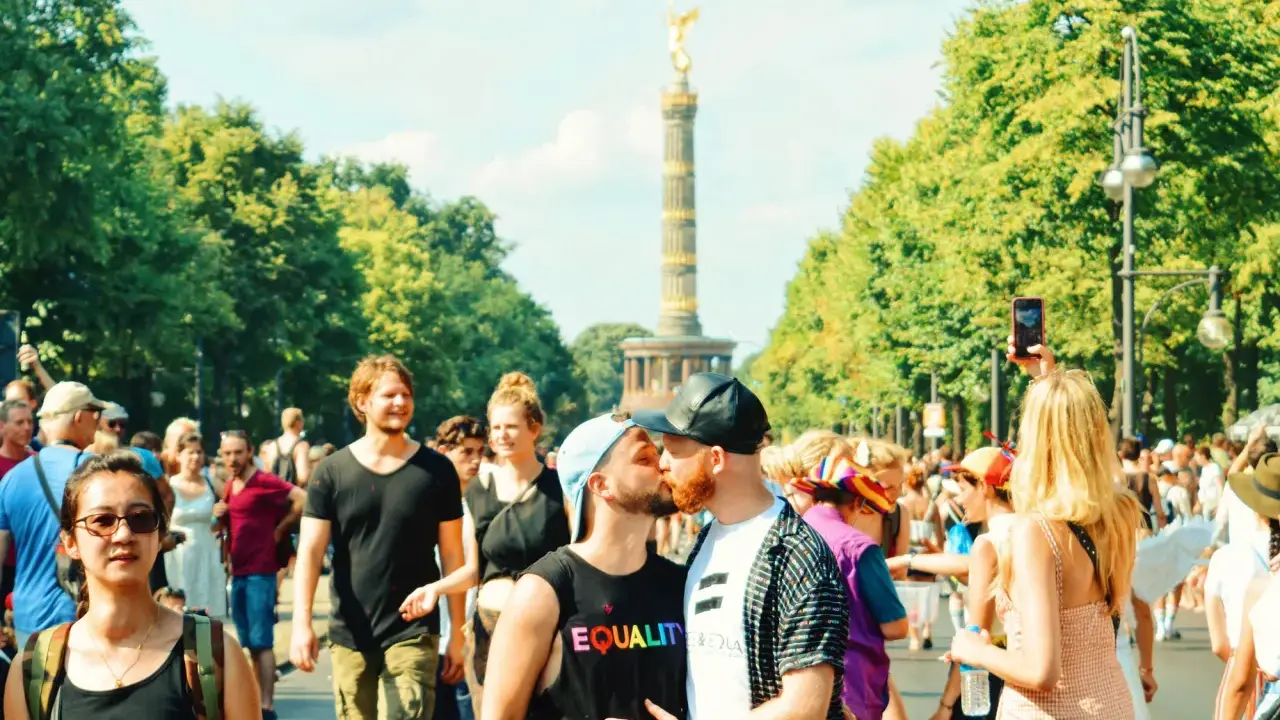 A couple kisses at a pride parade in Germany, with the Victory Column in the background. This scene shows Germany is gay friendly.