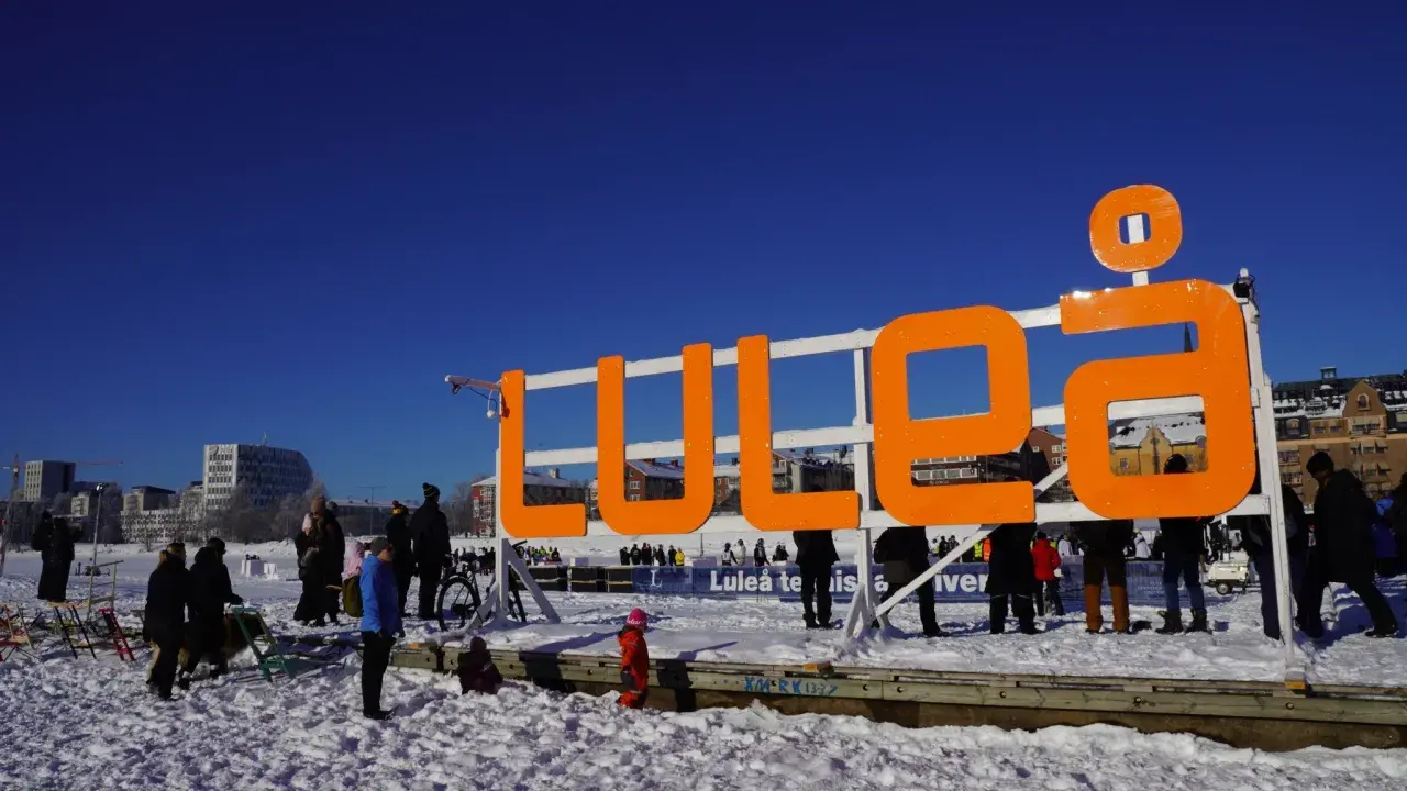 Stor orange skylt med texten "LULEÅ" i snöig miljö. Perfekt för luleå travel, en solig vinterdag.
