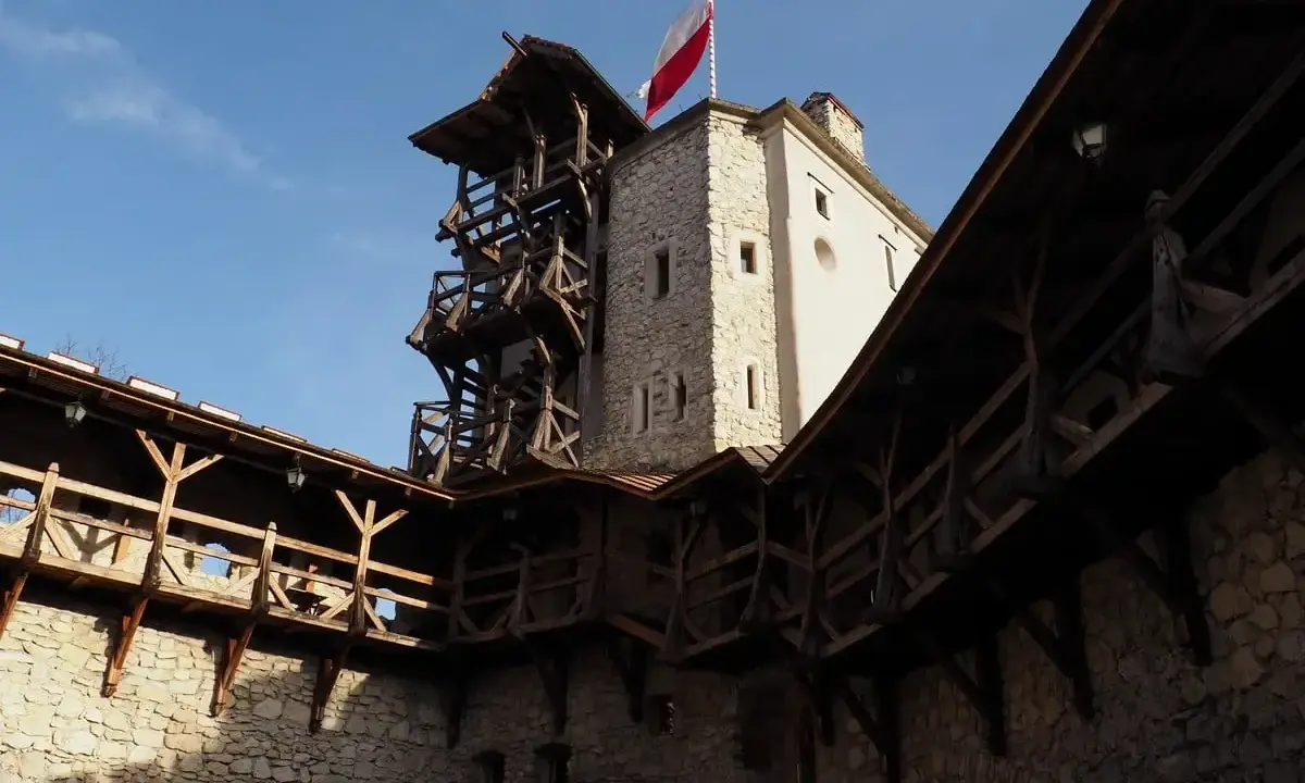 Zamek w Korzkwi z drewnianymi gankami i wieżą, na której powiewa polska flaga.