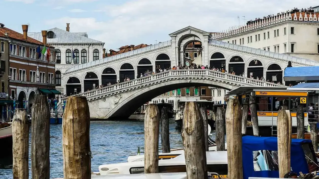 Le célèbre pont du Rialto à Venise, animé par des touristes, surplombe le Grand Canal où naviguent des gondoles et des taxis nautiques.