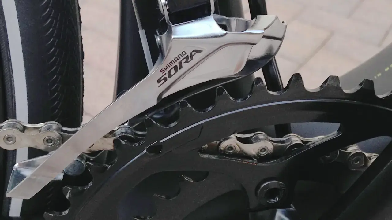 Montaż przedniej przerzutki Shimano Sora na rowerze. Widoczny fragment mechanizmu korbowego i łańcucha.