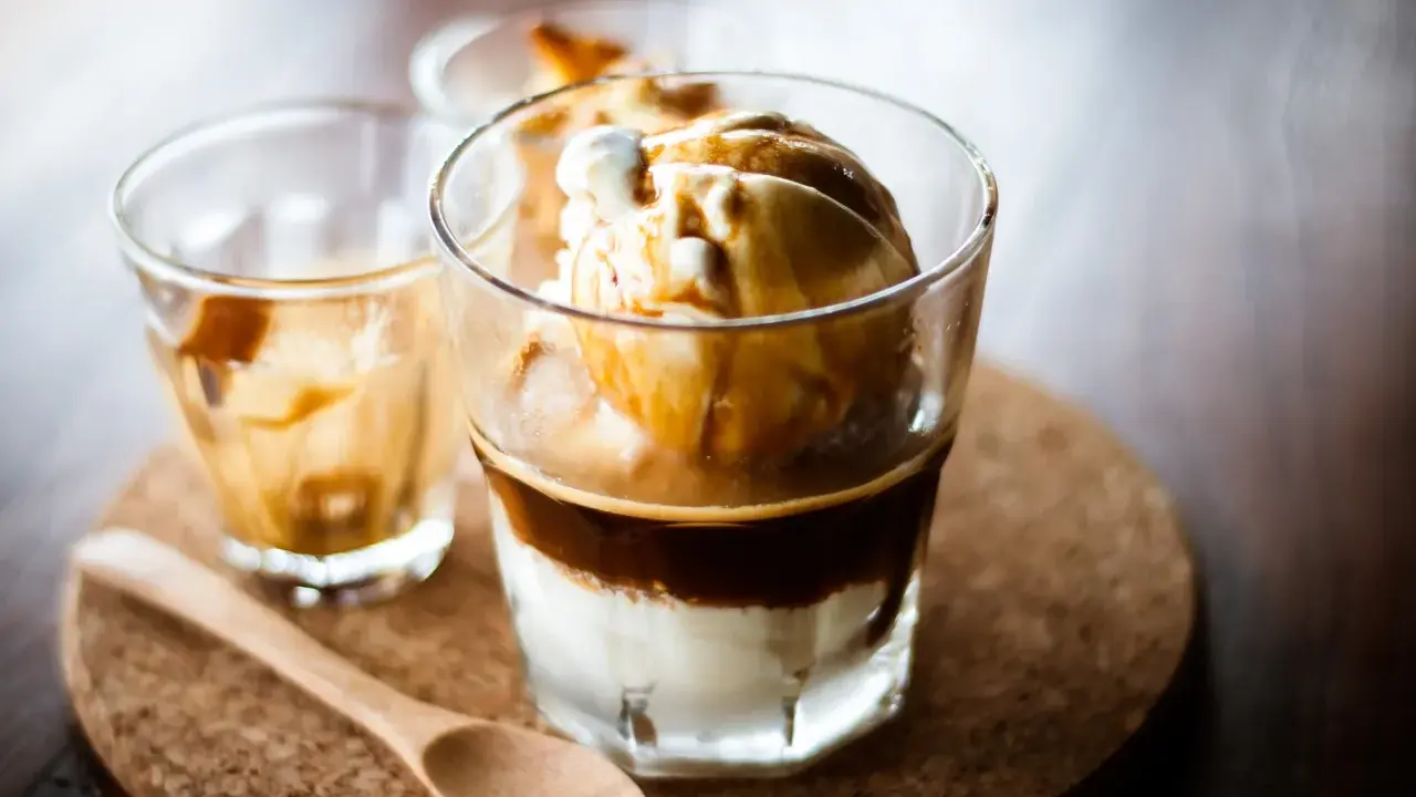 Ein italienischer Eiskaffee, Affogato, mit Vanilleeis und heißem Espresso. Ein Holzlöffel liegt daneben.