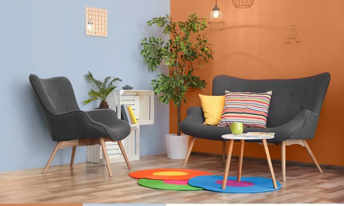 Nowoczesny salon z szarymi fotelami i kanapą, akcentem jest ściana w kolorze oranżowym.