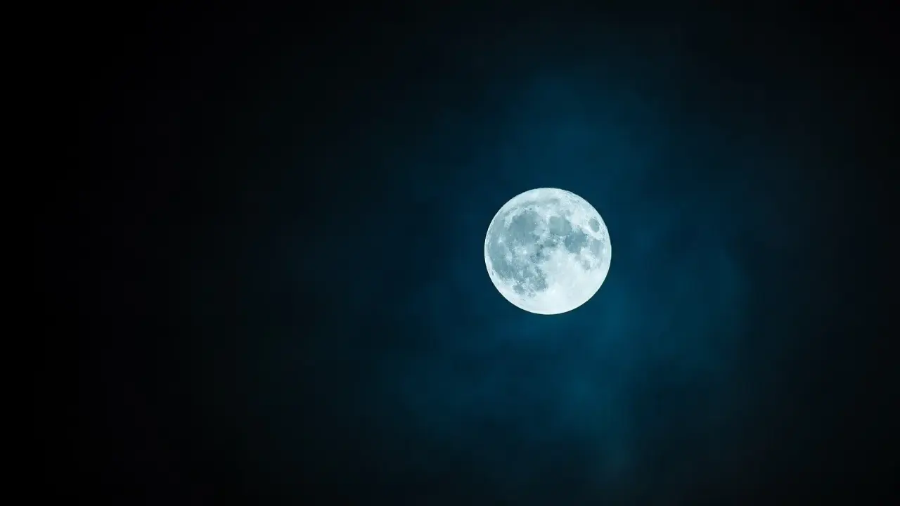 Jasny księżyc w pannie, otoczony mglistą poświatą, góruje na ciemnym, nocnym niebie.