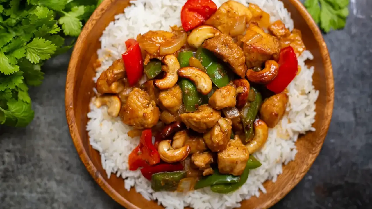Un délicieux poulet noix de cajou servi sur un lit de riz blanc. Des poivrons rouges et verts ajoutent de la couleur à ce plat savoureux.