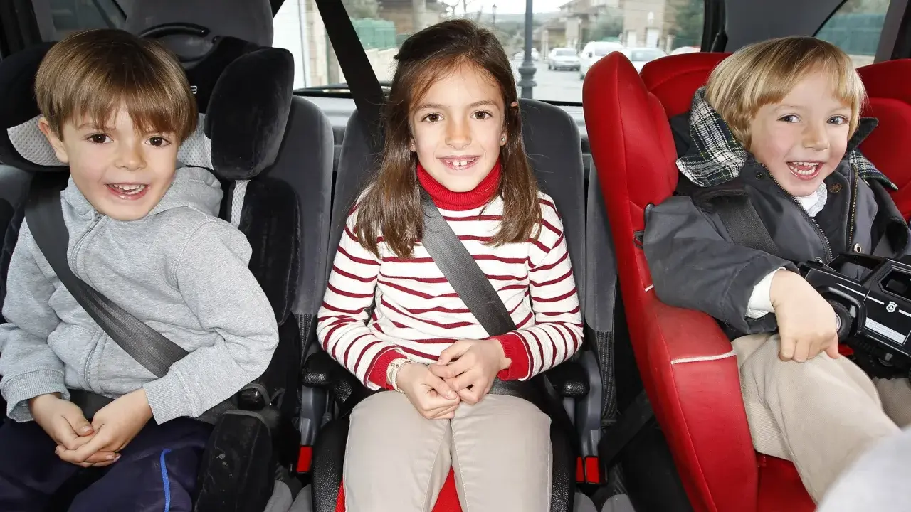 Tres niños sonríen en sus asientos de coche, listos para viajes en coche con niños de 2 años.