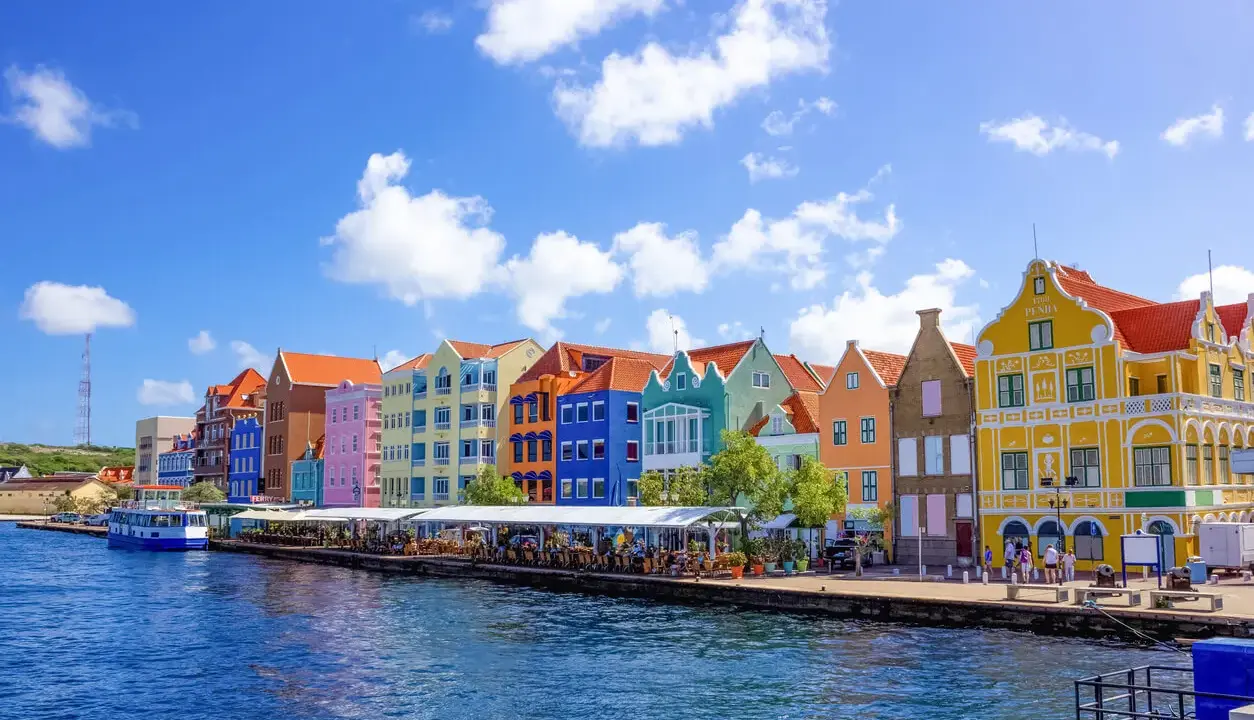 Färgstarka hus längs en kaj, en båt i vattnet. Här kan man se var ligger Curacao, en karibisk pärla.