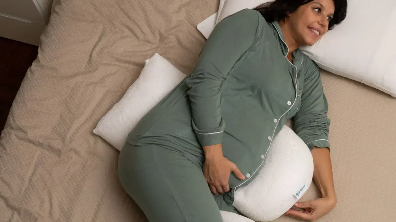 Donna incinta, con pigiama verde, si rilassa a letto con un cuscino di supporto, alleviando la stanchezza in gravidanza.