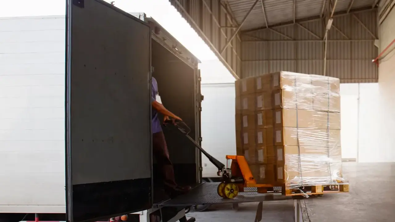 Un operario usa una carretilla para el transporte de materiales, cargando cajas en un camión.
