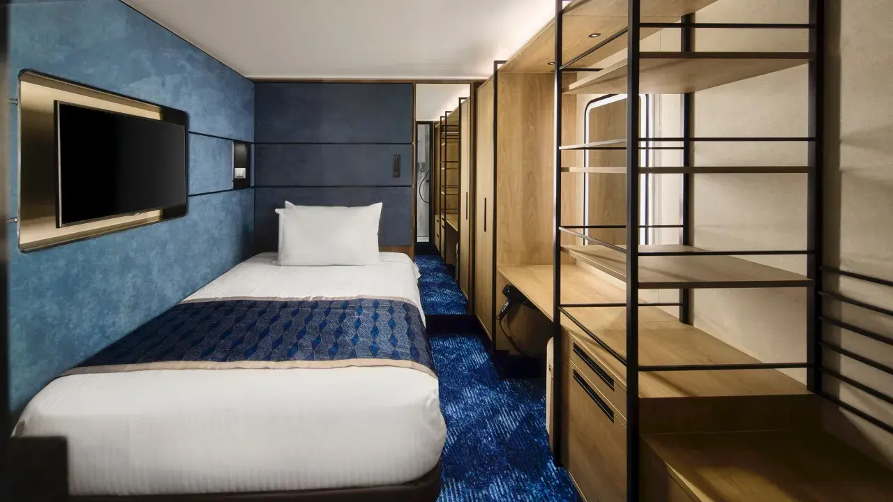 Interno cabina singola nave da crociera: letto, TV a parete, armadio aperto con mensole e scrivania. Le dimensioni delle cabine sono ottimizzate per il comfort.