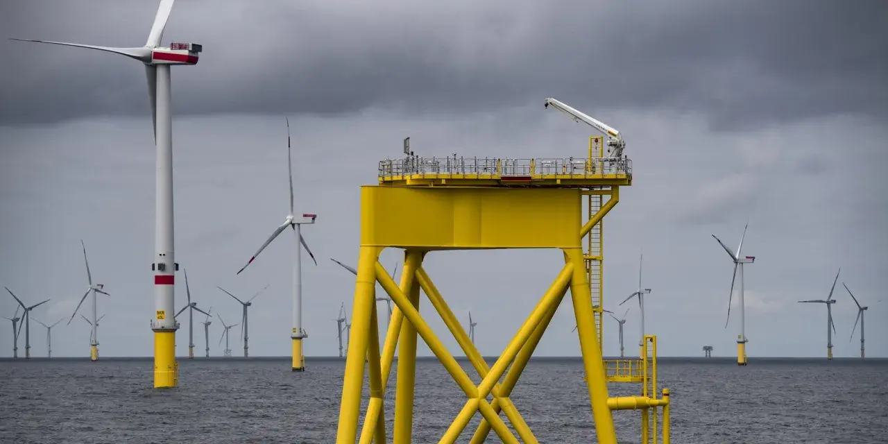 Große gelbe Plattform mit Kran inmitten vieler Windkraftanlagen im Meer. Die Zukunft der Windkraft onshore und offshore.