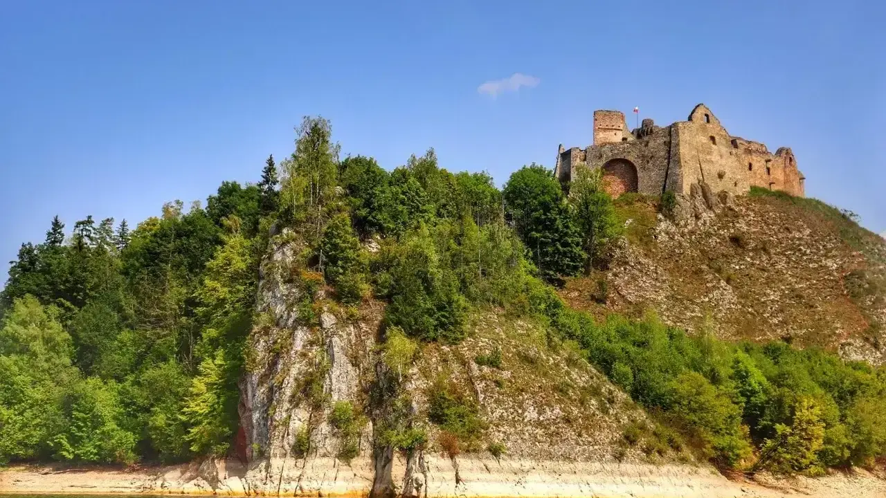 Zamek Czorsztyn góruje nad jeziorem, otoczony zielenią. Ruiny zamku na skale, widok z wody.
