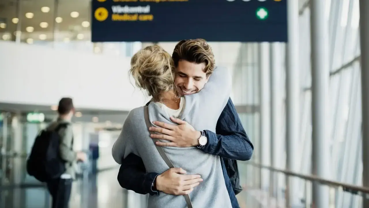 Glädjefylld återförening på en av Sveriges internationella flygplatser. Ett par kramas varmt i terminalen.