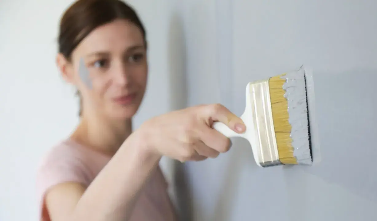 Une femme effectue une retouche peinture murale avec un pinceau gris. Une tache de peinture grise est visible sur sa joue.