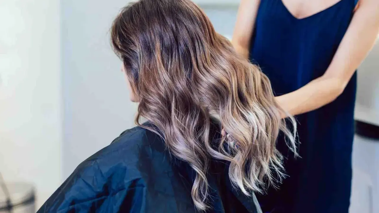 Kobieta z falowanymi włosami w technice baleyage blond, z subtelnymi refleksami przechodzącymi w jaśniejsze odcienie.