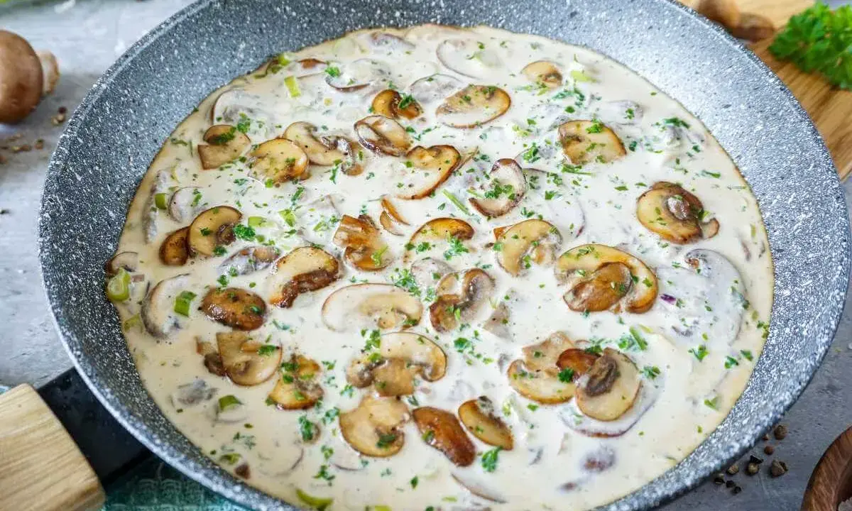 Cremige Rahmsauce mit frischen Champignons, verfeinert mit Petersilie, in einer Pfanne.